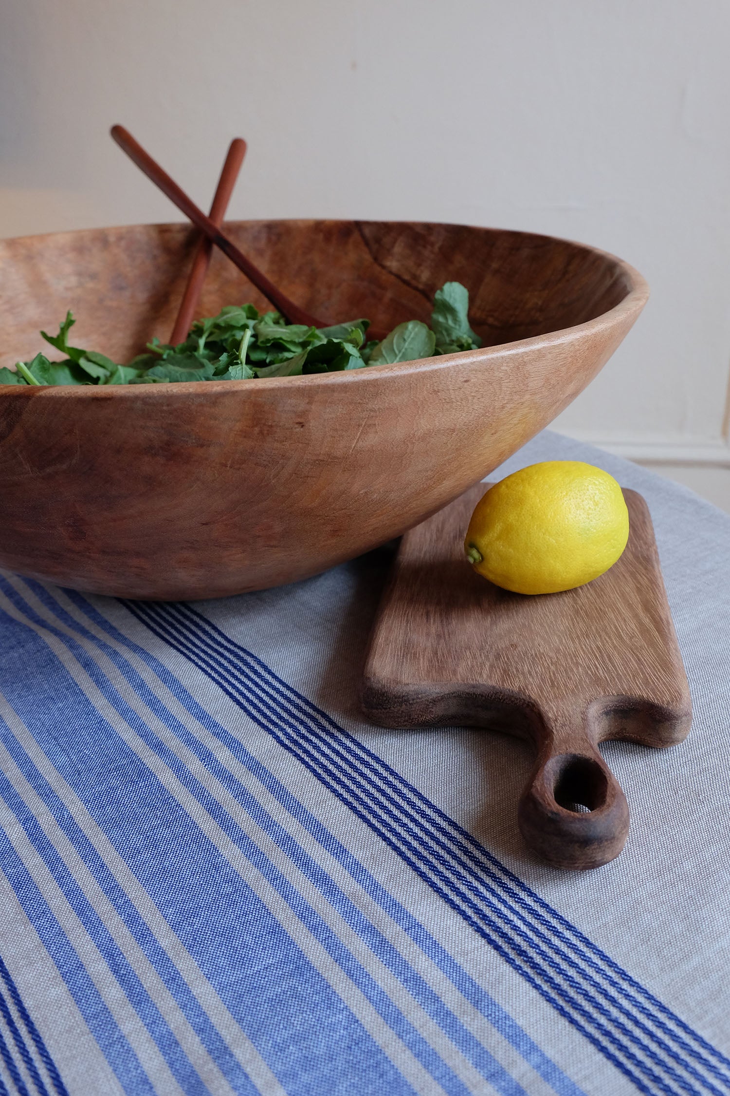 Sobremesa wooden salad bowl, serving spoons, and cutting board on a blue chambray table runner