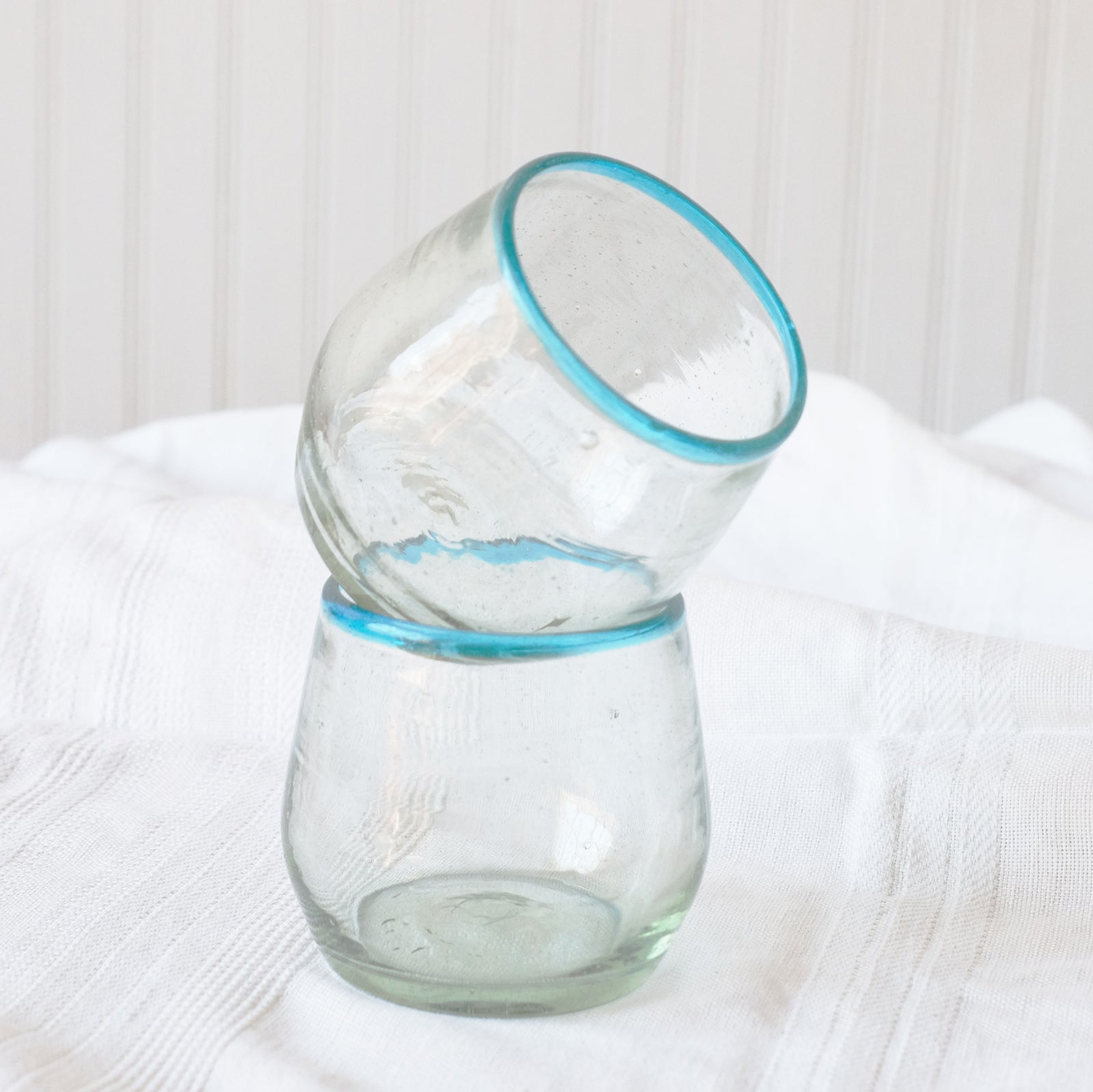 Two hand blown glasses stacked. Glasses are handblown, made from recycled glass in Guatemala. Wine glasses are clear with an aqua colored rim. Simple elegance.
